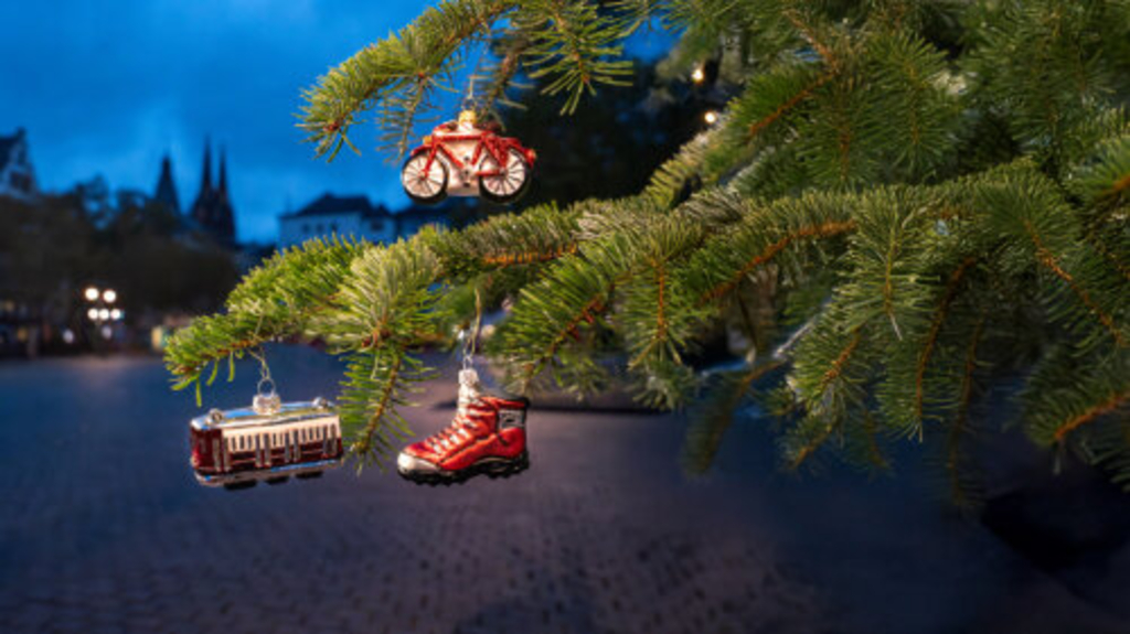 Im Vordergrund sieht man Tannenzweige eines Weihnachtsbaums an denen drei Anhänger in Form einer Bahn, eines Fußes und eines Fahrrades hängen. Im Hintergrund sind die Domspitzen zu sehen., Link auf Verkehrsinformationen für die Adventszeit