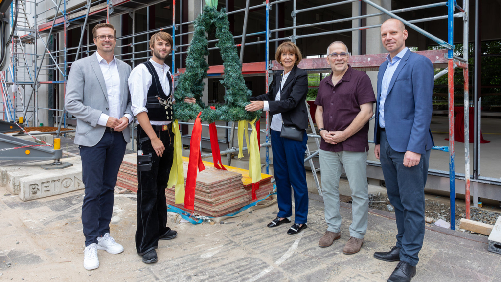 Andree Haack (Dezernent für Stadtentwicklung, Wirtschaft, Digitalisierung und Regionales), Zimmerermeister Max Berheide, Oberbürgermeisterin Henriette Recker, Martin Süsterhenn (Schulleiter) und Tim Schneider (Geschäftsführer Fechtelkord & Eggersmann) mit dem Richtkranz