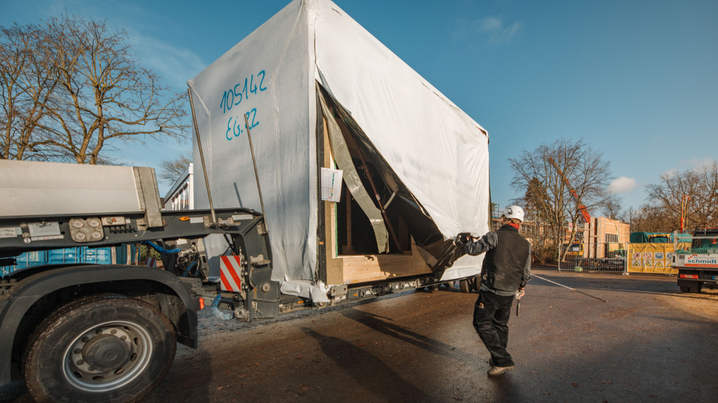 Ein Holzmodul ist auf einem Schwerlasttransporter angekommen und wird von seiner Schutzfolie befreit.