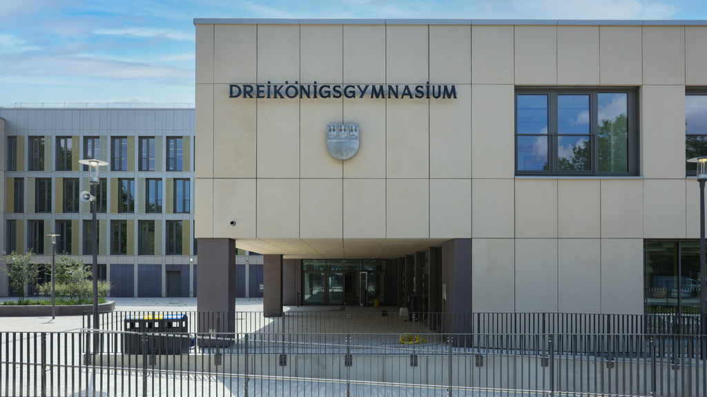 Haupteingang der Schule mit dem Schriftzug "Dreikönigsgymnasium" sowie einem Stadtwappen. Davor ist eine Rampenanlage zu erkennen.