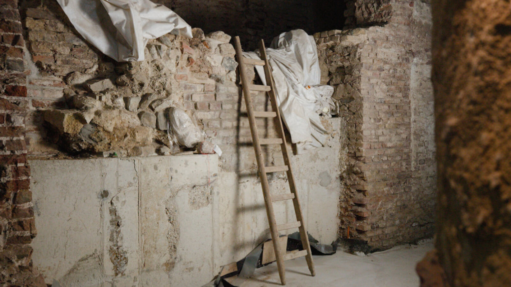 Historische Mauern mit einer Unterfangung aus Beton im Goldschmiedeviertel in der Archäologischen Zone. Davor steht eine Holzleiter, die Mauern sind mit Vlies geschützt.