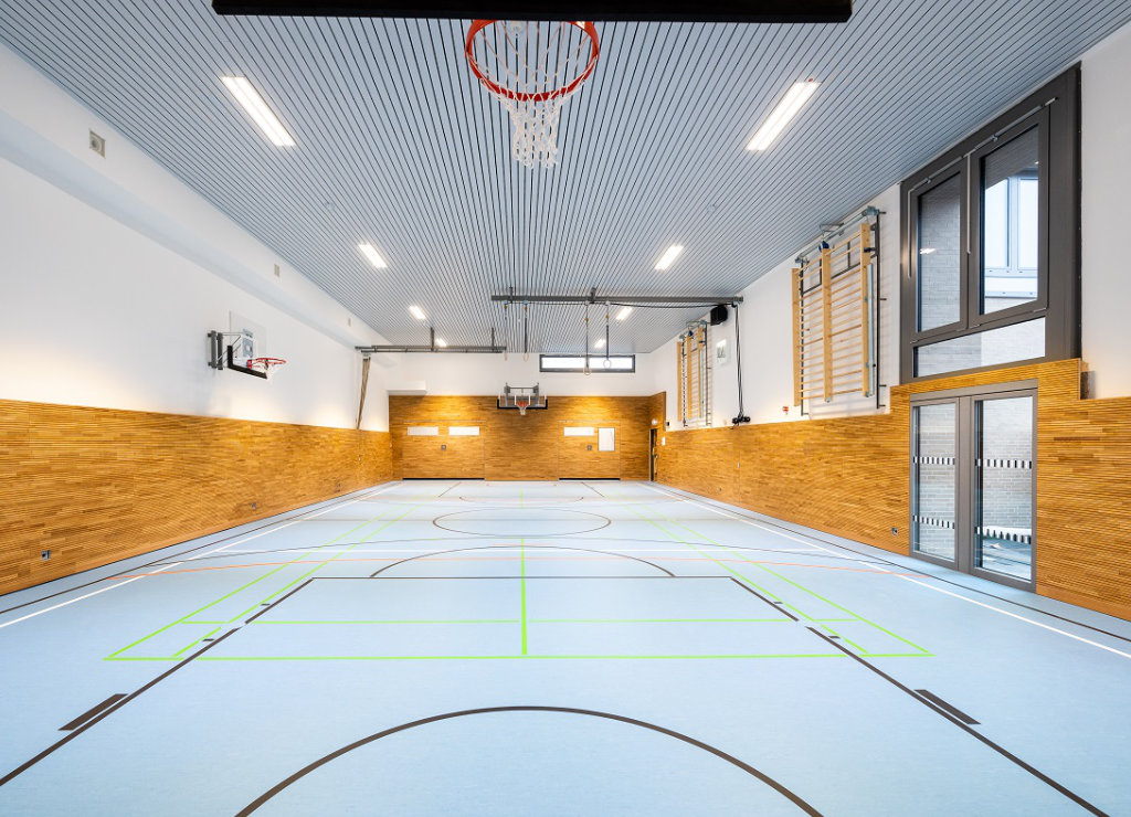 Gymnastikraum mit Prallschutz aus Holzlamellen, Basketballkörben und an der Wand montierten Sprossenwänden