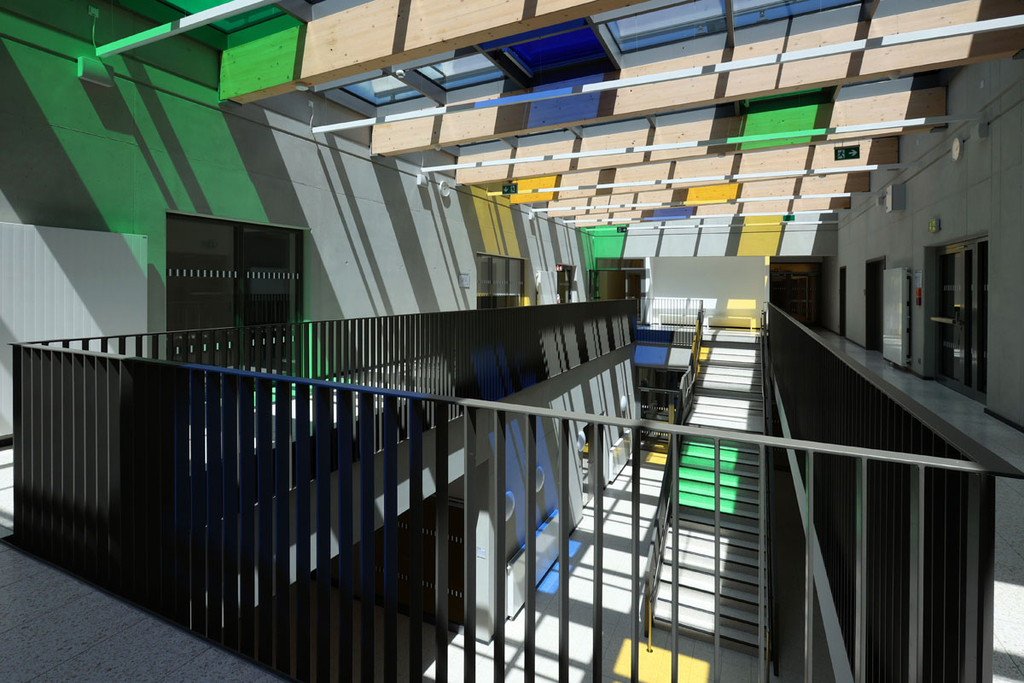 Durch das teilweise bunte Glasdach wirft die Sonne grün, blaue oder gelbe Lichtstrahlen durch die offene Galerie bis in die Erschließungshalle