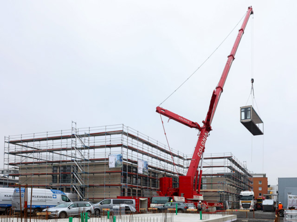 Ein Kran befördert ein Modulbauteil durch die Luft an die richtige Stelle.