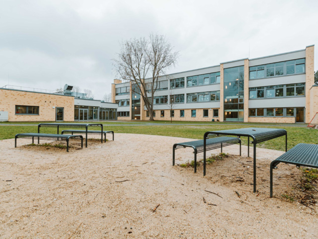 Pausenplätze in der grünen Außenanlage mit Blick auf die Mensa und den Erweiterungsneubau