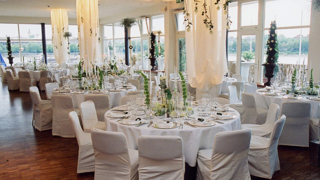 Festlich geschmückter Parksaal. Zu sehen sind eingedeckte runde Tische und mit Hussen überzogene Stühle.