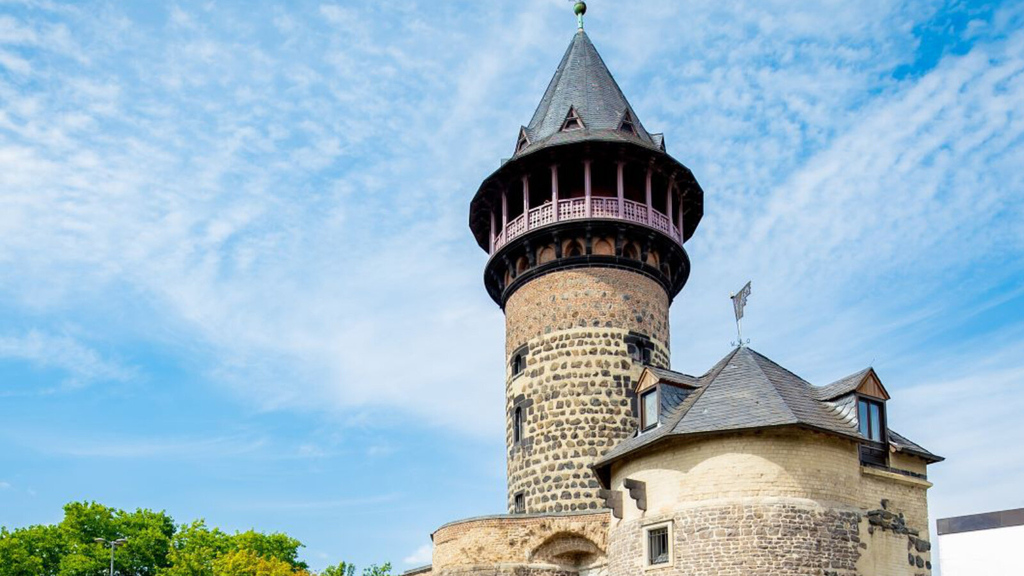 Außenansicht der Ulrepforte. Zu sehen sind histroische Bauwerke in verschiedenen Größen. Als größtes Bauwerk ist die Ulrepforte mit spitzem Dach abgebildet.