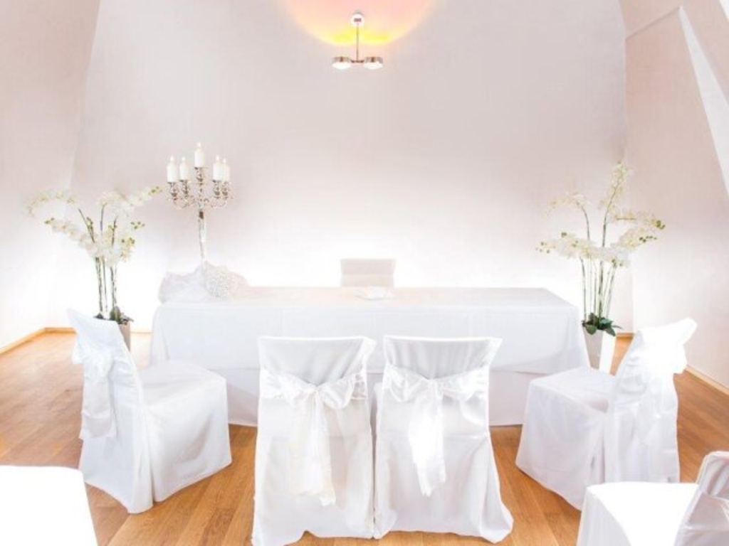 Bel Etage im Schokoladenmuseum. Zu sehen ist ein Trautisch mit weißer Tischdecke, vier Stühle mit weißen Hussen, Pflanzen und Kerzenständer. 