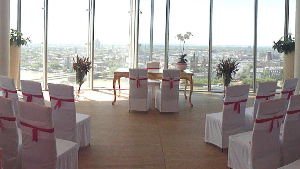 Trauzimmer über den Dächern von Köln. Zu sehen ist ein festlich geschmückter Trautisch und Stühle für die Gäste mit weißen Hussen