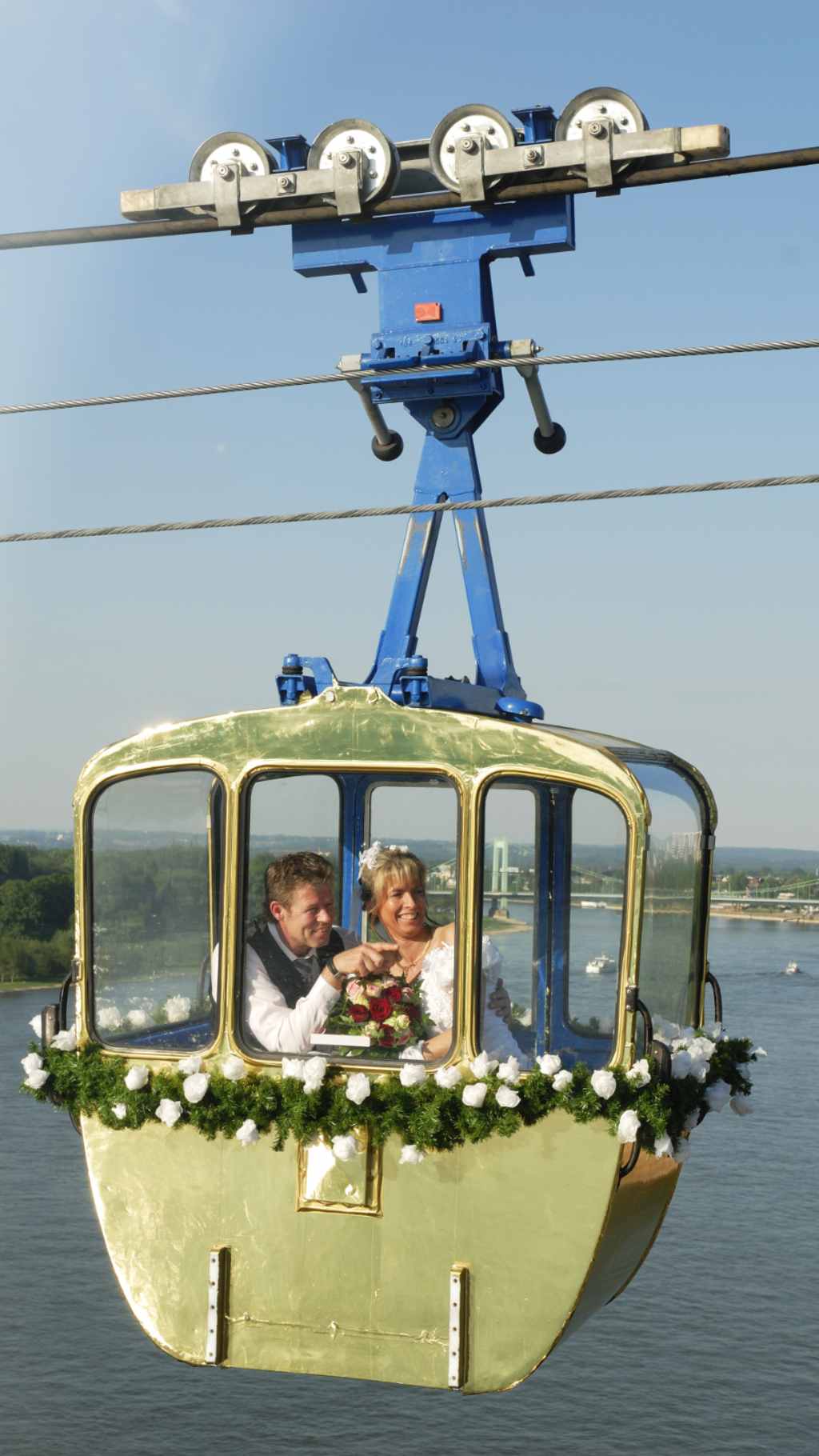 Ein Hochzeitspaar sitzt in der geschmückten Rheinseilbahn hoch über dem Rhein.