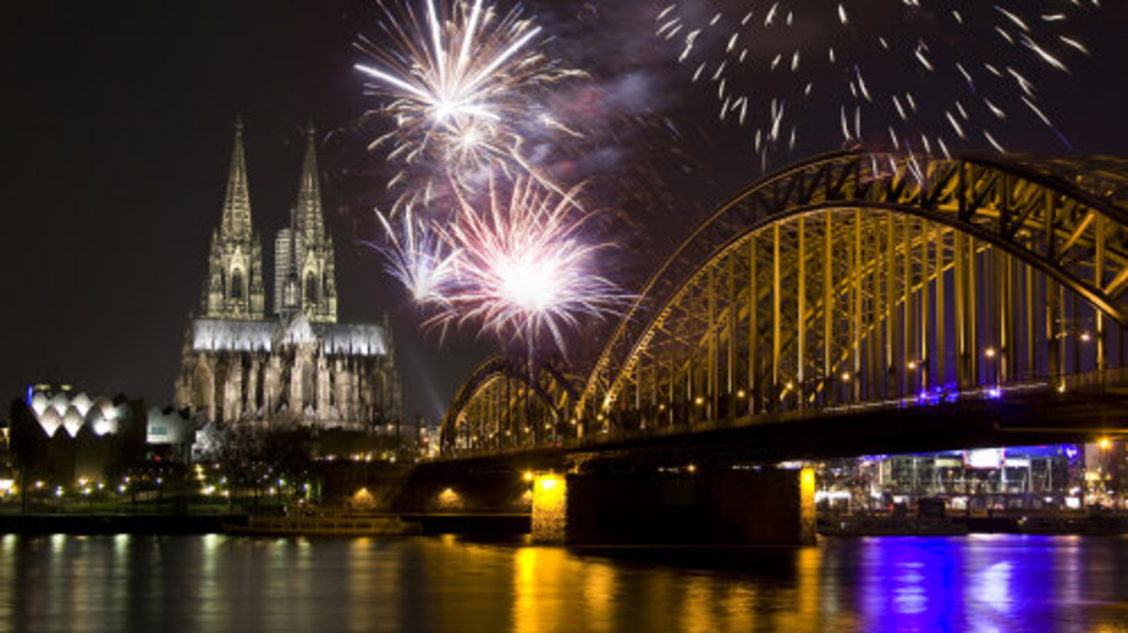 Silvesterfeuerwerk in Köln. Zu sehen sind mehrere bunte Feuerwerkraketen. Beleuchtet ist der Kölner Dom und die Hohenzollernbrücke., Link auf Sperrungen an Silvester