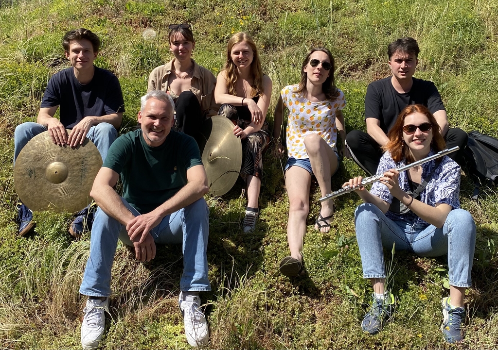 Sieben Musiker*innen sitzen mit Ihren Instrumenten auf einer Wiese