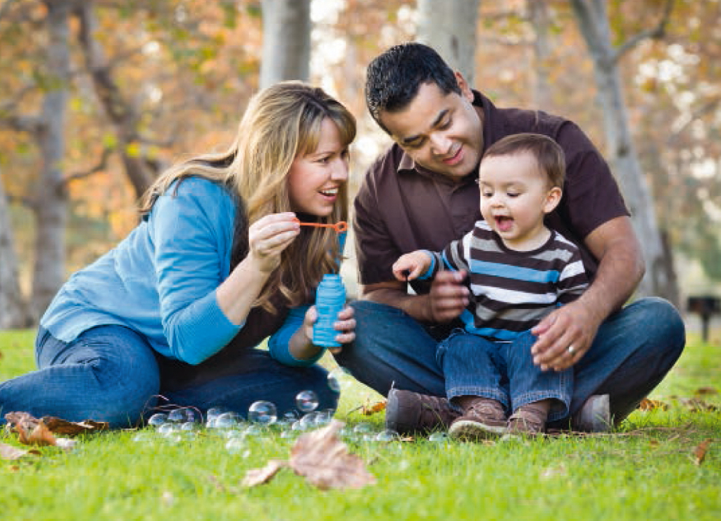 Familie sitzend im Gras und mit dem Kind spielend