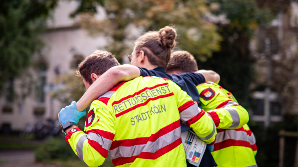 Zwei Auszubildende zum Notfallsanitäter helfen einem Verletzten im Rahmen einer Übung., Link auf Ausbildung zum*zur Notfallsanitäter*in