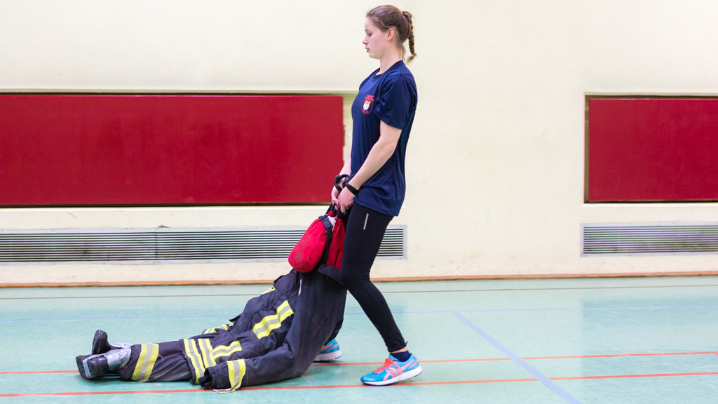 Frau zieht eine Übungspuppe. , Link auf Eignungstest für Brandreferendar*innen und Brandoberinspektor*innen