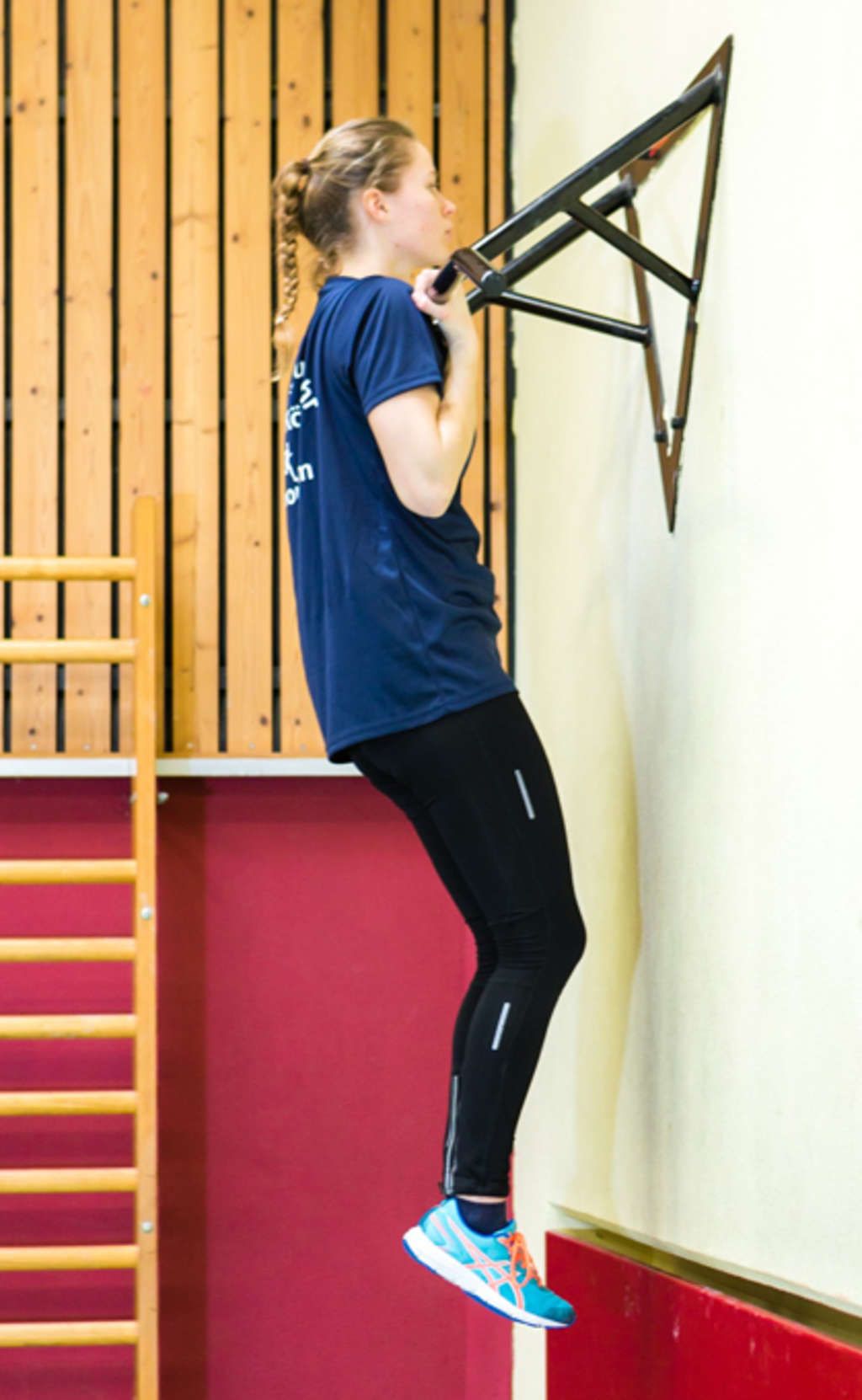 Frau hängt im Kammgriff (Untergriff) an einer Klimmzugstange.