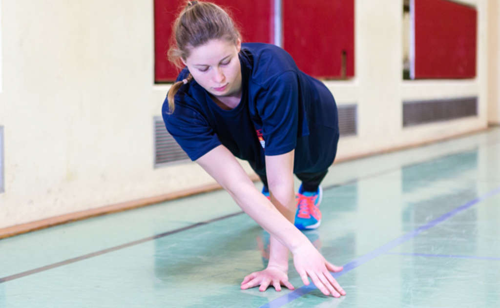 Frau in Liegestützhaltung übergreift mit der rechten Hand die linke Hand.