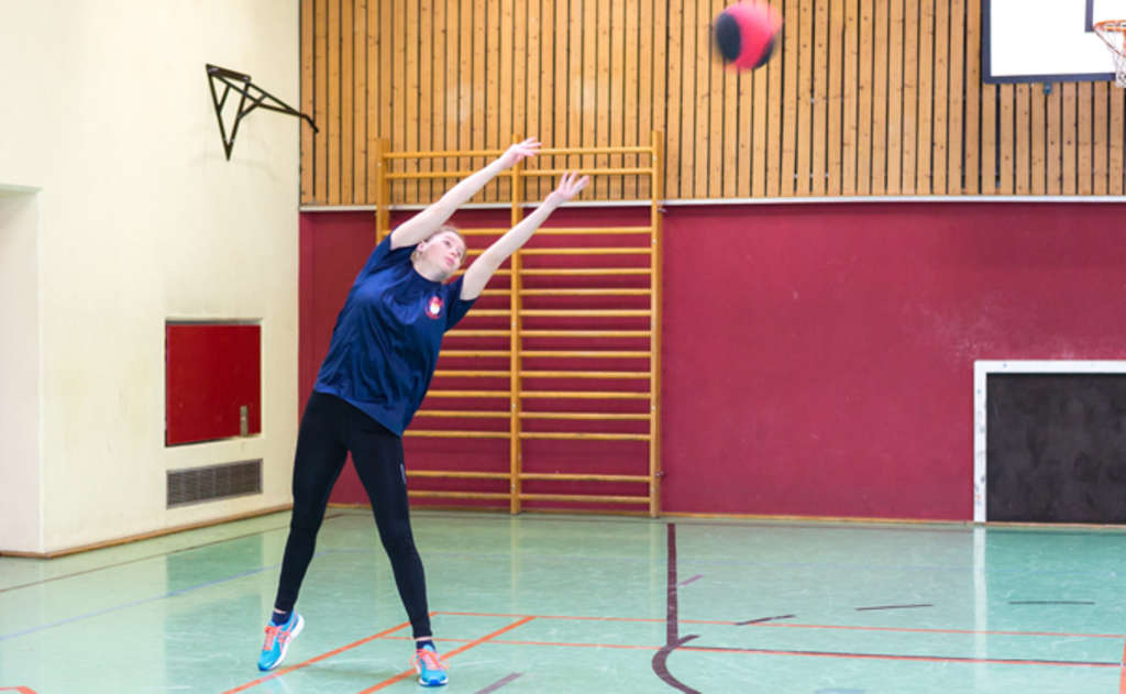 Frau wirft beidhändig einen Medizinball in seitlicher Wurfbewegung.