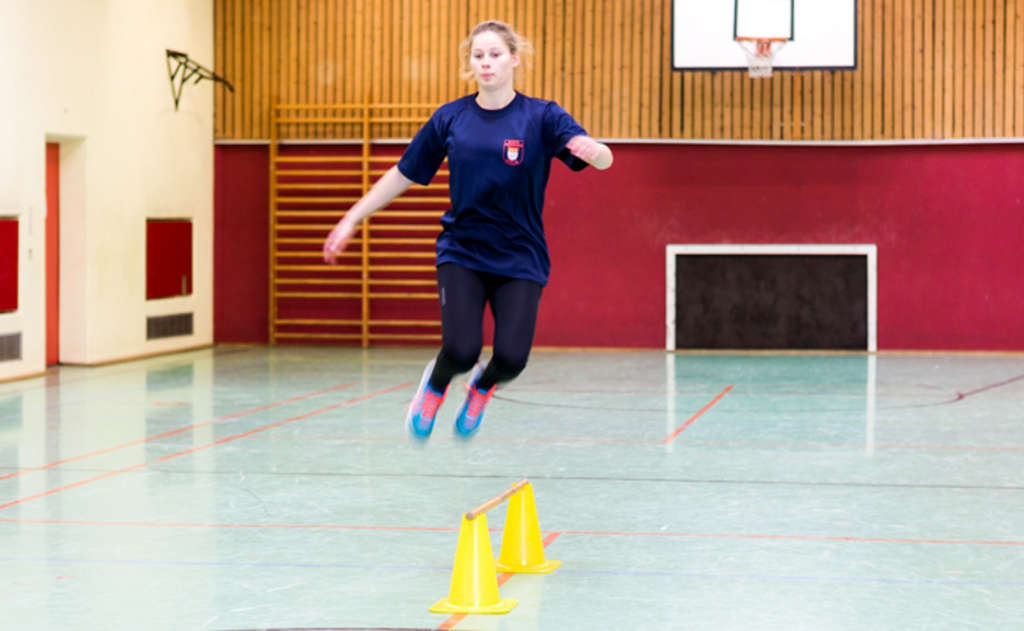 Frau macht Wechselsprünge über eine Stange