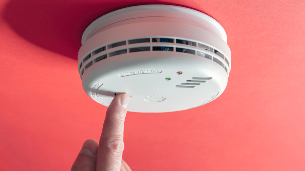 Rauchmelder unter der Decke. Mit einem Fingerdruck versucth eine Person zu testen, ob die Batterie noch funktioniert.