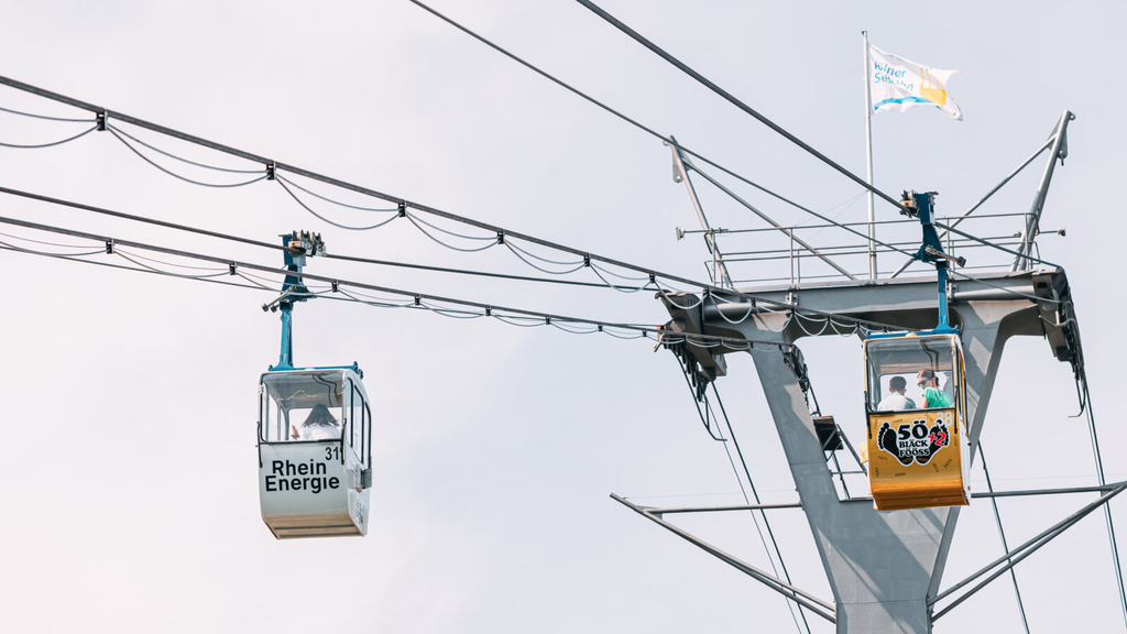 Kölner Rheinseilbahn - Zu sehen sind zwei Gondeln in denen Personen sitzen.