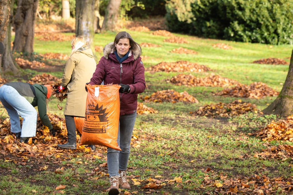 Frau trägt einen mit Laub gefüllten orangenen Sack.