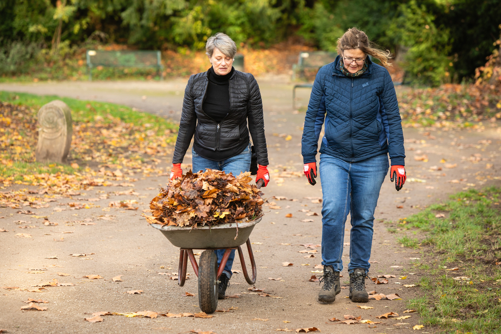 Zwei Frauen schieben eine mit Laub gefüllte Schubkarre.