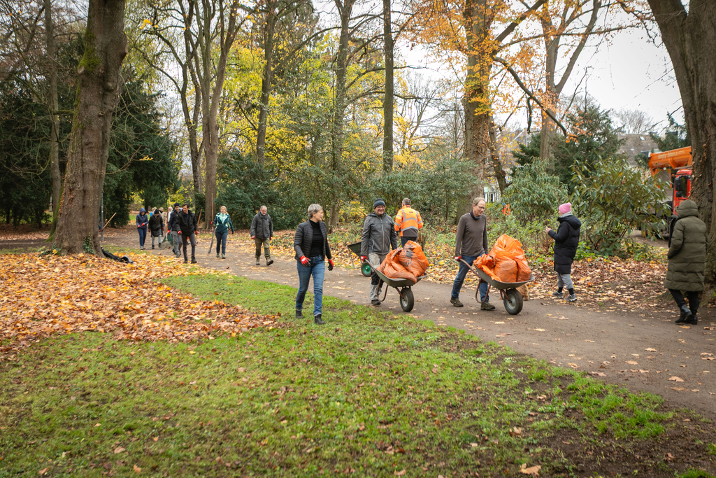 Personen schieben Schubkarren über einen Parkweg.
