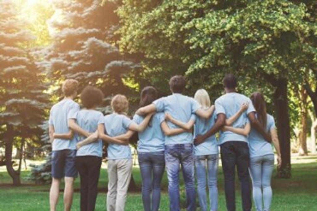 Eine Gruppe von Ehrenamtlichen die sich im Park umarmen. Rückansicht, Link auf Integration und Interkulturelles - Stadt Köln