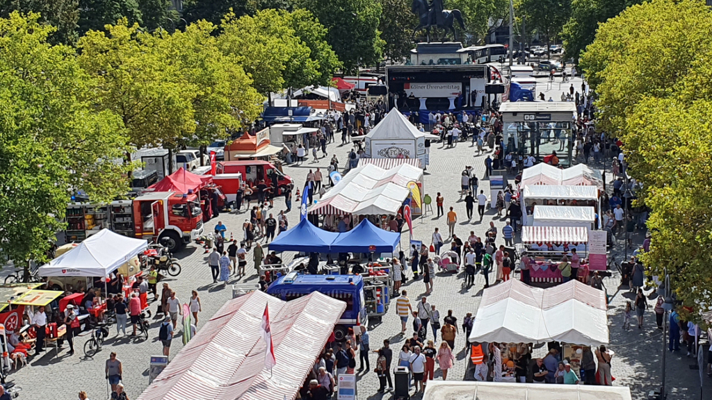 Blick von oben auf den Heumarkt auf dem viele Menschen zwischen Informationsständen und der Hauptbühne zum Ehrenamtstag 2022 schlendern, Link auf Kölner Ehrenamtstag 2024 - Stadt Köln