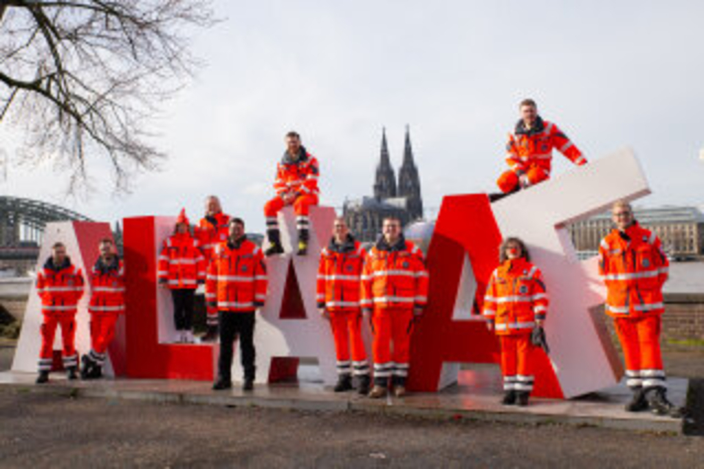auffällig große 3D-Buchstaben in rot und weiß als Fotospot bilden den Schriftzug "ALAAF“. Ehrenamtliche der Johanniter-Unfall-Hilfe positionieren sich um und auf den Buchstaben. Im Hintergrund sieht man den Kölner Dom. , Link auf Johanniter-Unfall-Hilfe e. V.
