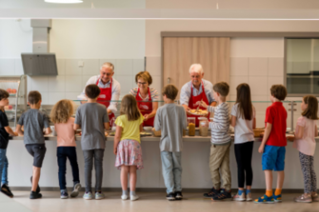 Foto drei Ehrenamtliche teilen in einer Kantnine Essen an kleine Kinder aus. 