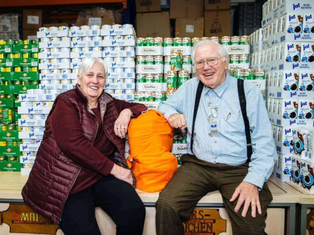 Die Verantwortlichen des Vereins sitzen vor einem Berg mit Konservendosen, zwischen ihnen ein orangefarbener Sack gefüllt mit Lebensmitteln.