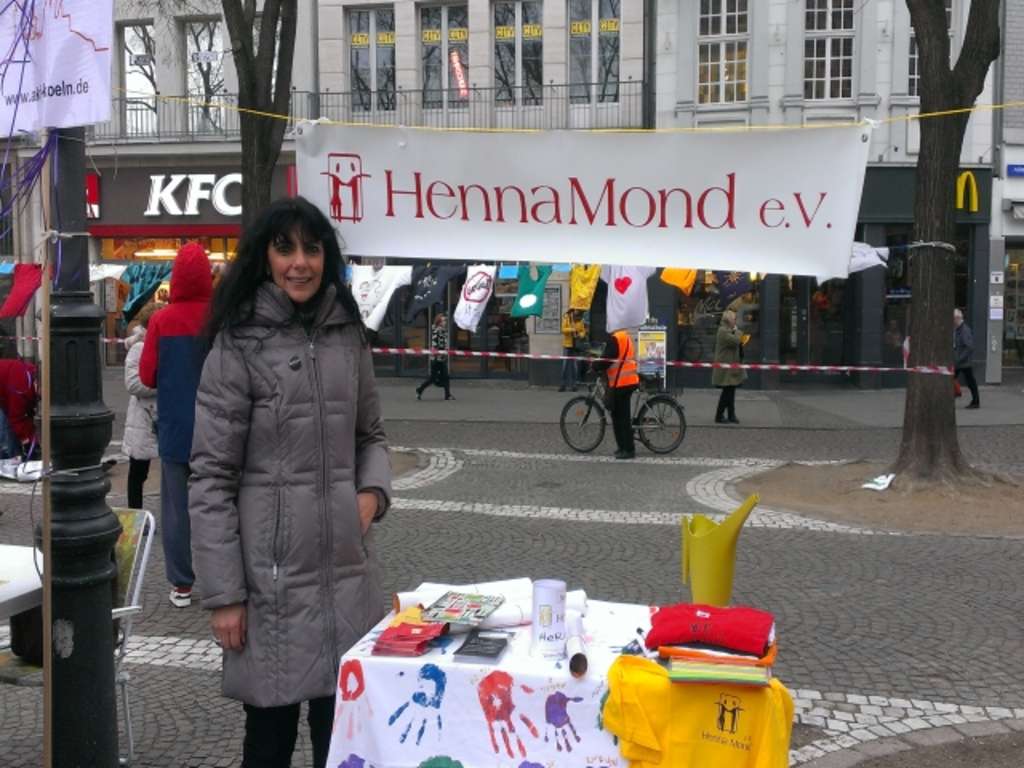 Eine Frau steht vor dem Infostand von HennaMond e.V. auf einem Marktplatz