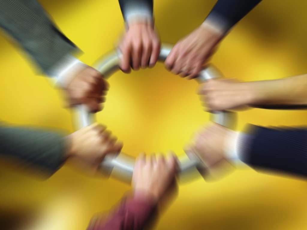 Sieben Hände halten gemeinsam einen Ring fest. Der Hintergrund ist gelb.