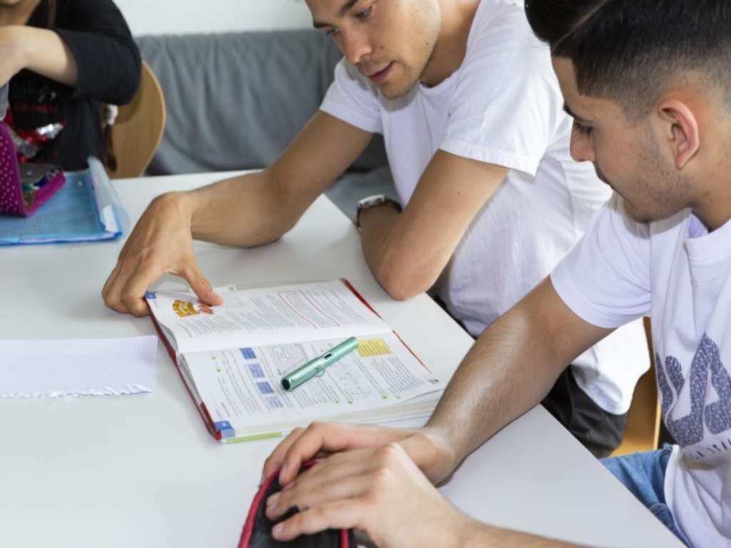 zwei jugendliche Migranten sitzen an einem Tisch und lernen. Vor Ihnen liegt ein Schulbuch.