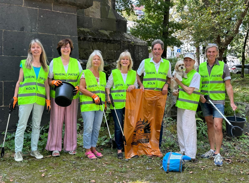 Sieben Rheinpat*innen, ausgestattet mit Greifzange, Müllbeutel und gelber Warnweste mit der Aufschrift „Rheinpaten Köln“