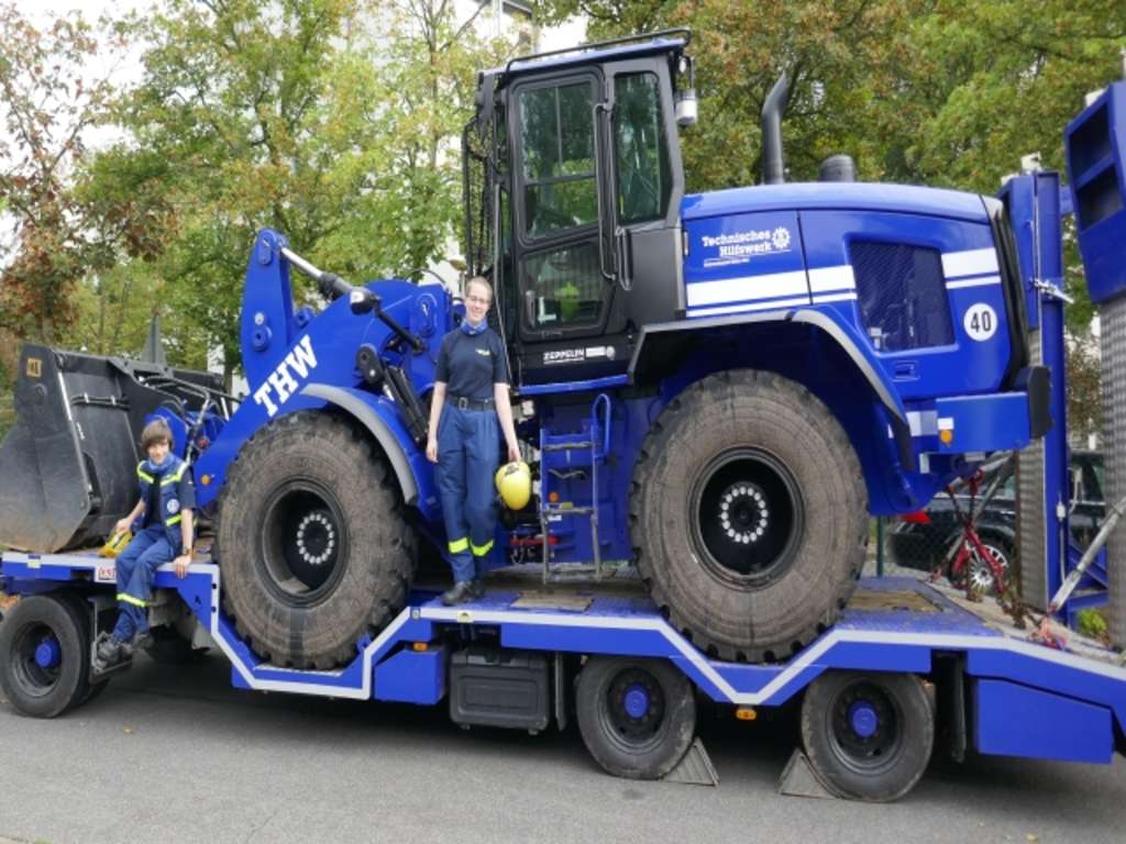 zwei JungeFreiwillige des THW vor einem großen Bagger des THW