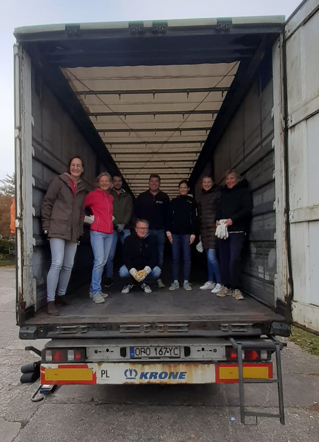 Acht Personen stehen auf der Ladefläche eines leeren Lastkraftwagens