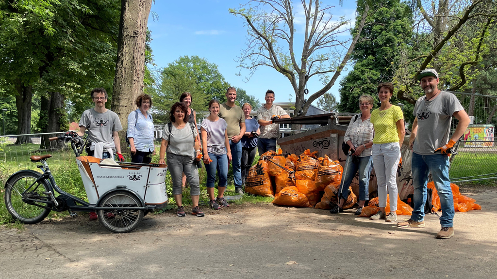 Elf Freiwillige aufgestellt zum Gruppenfoto. Mittig zahlreiche gefüllte orange Müllsäcke vor einem Container