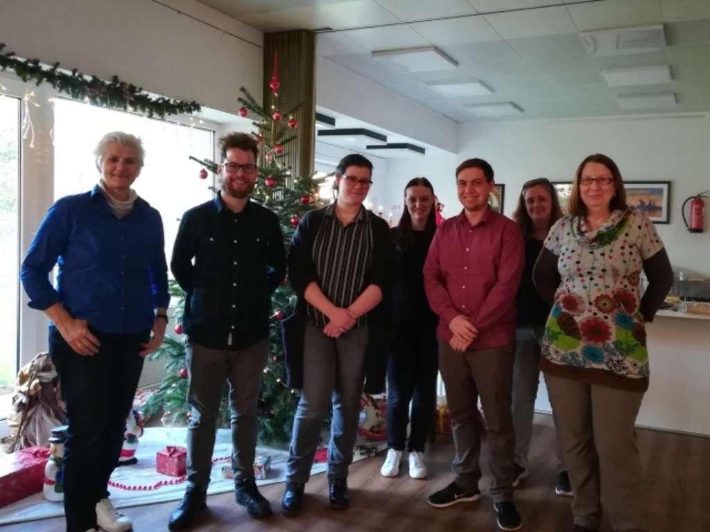 Sieben fleißige Helferinnen und Helfer der Stadt Köln stehen in einem Wohnzimmer vor einem Tannenbaum.