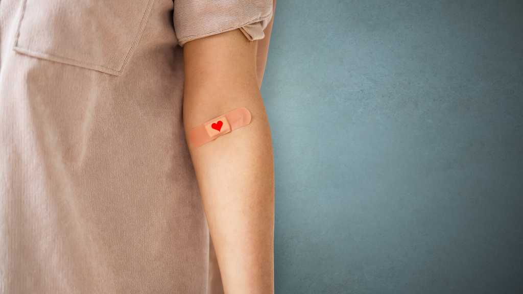 Eine Person mit Pflaster in der Armbeuge, darauf ein gemaltes rotes Herz.