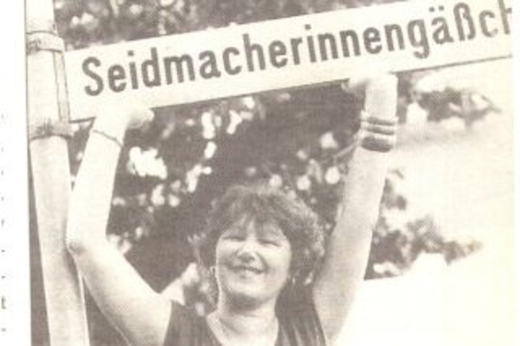 Foto eines Zeitungsbilds, eine Frau "stützt" lachend das Straßenschild des Seidmacherinnengäßchens, Link auf Herkunft der Kölner Straßennamen - Stadt Köln
