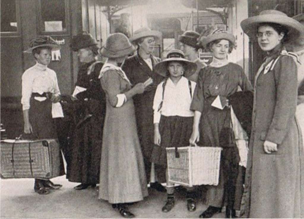Sieben Frauen in Reisekleidung mit Koffern, etwa zu Beginn des 20. Jahrhunderts