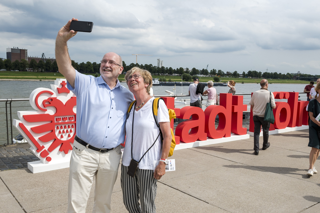 Foto von einem Mann und einer Frau, wie sie vor einem Stadt Köln Aufsteller ein Selfie machen