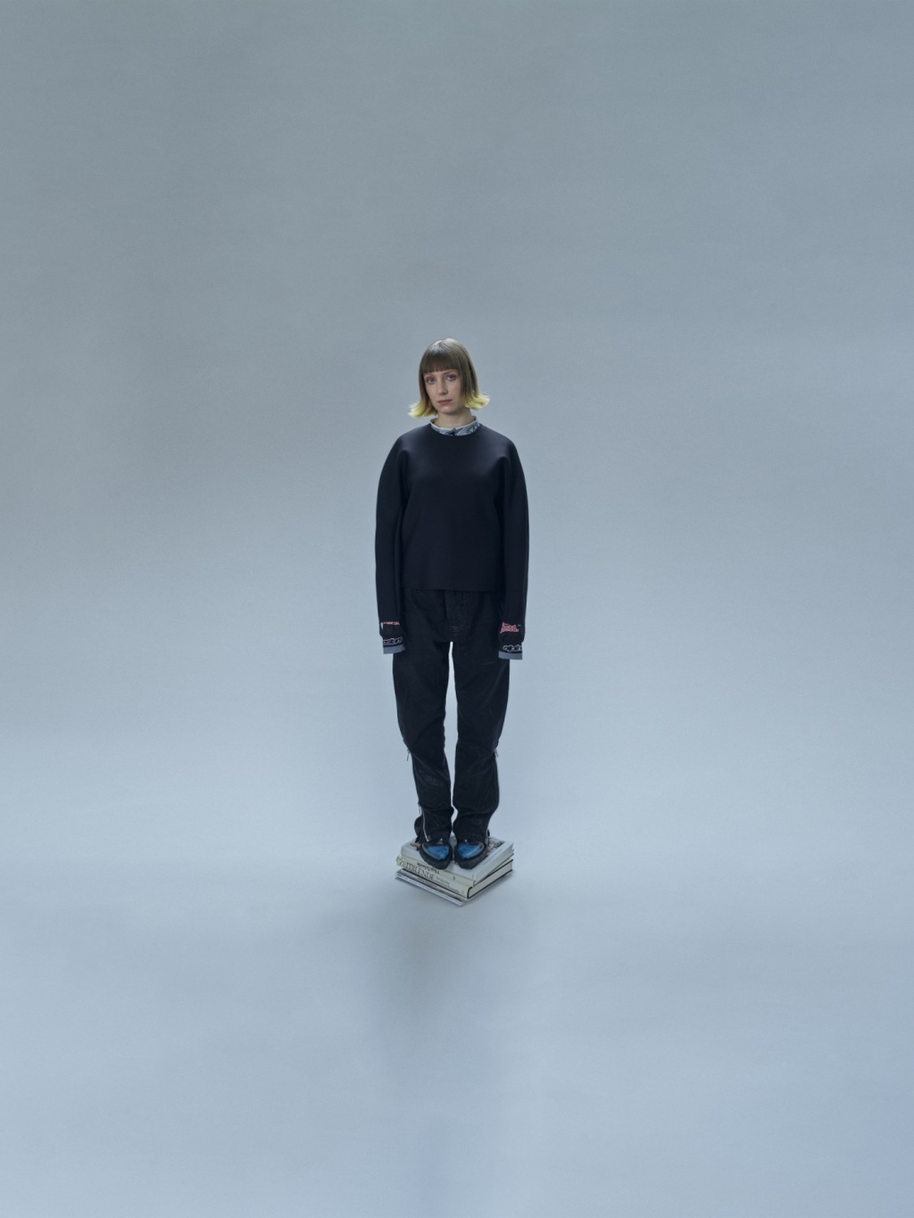 Ein Foto der Künstlerin IUMA, die auf einem Stapel Bücher steht