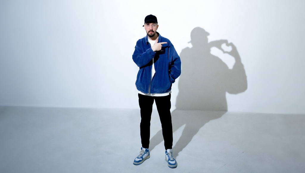 Der Künstler Nico Gomeze ist abgebildet, wie er auf seinen Schatten zeigt. Der Schatten zeigt ein Herz mit seinen Händen.