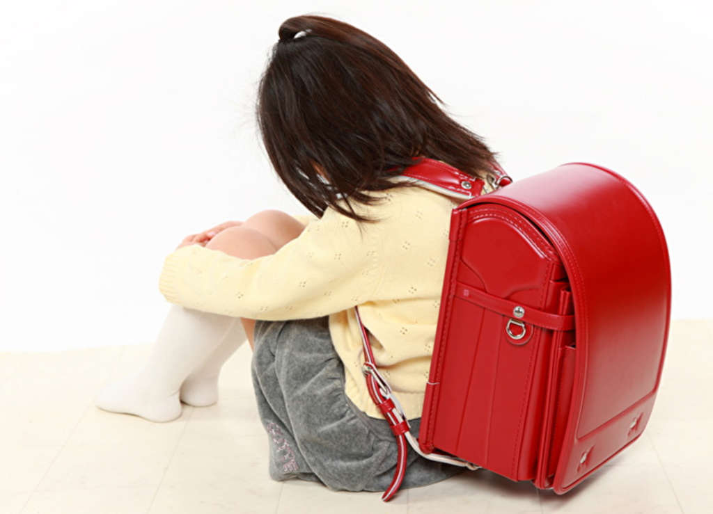 Kind mit Schulranzen sitzt auf dem Boden