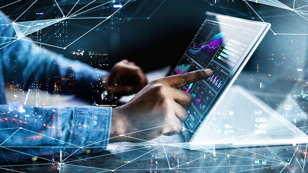 Ein Mann mit Jeanshemd tippt auf einem Notebook, auf dem Grafiken und Analysen zu sehen sind.