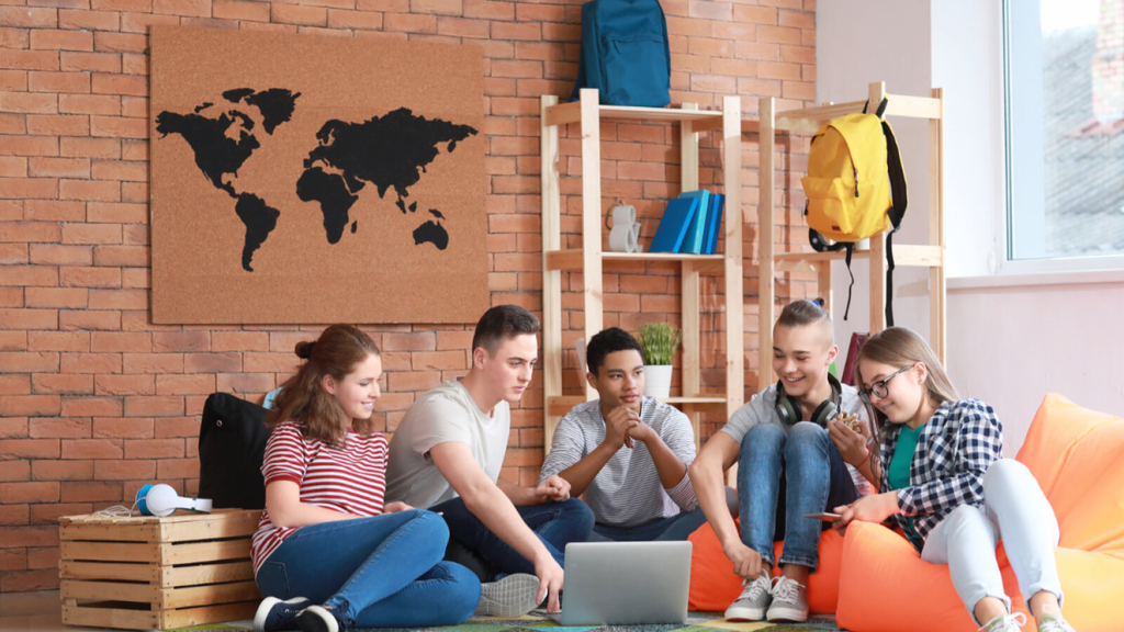 Gruppe Jugendlicher verbringen gemeinsam Zeit miteinander, sitzend auf dem Boden und Sitzsäcken., Link auf Angebote für Kinder und Jugendliche